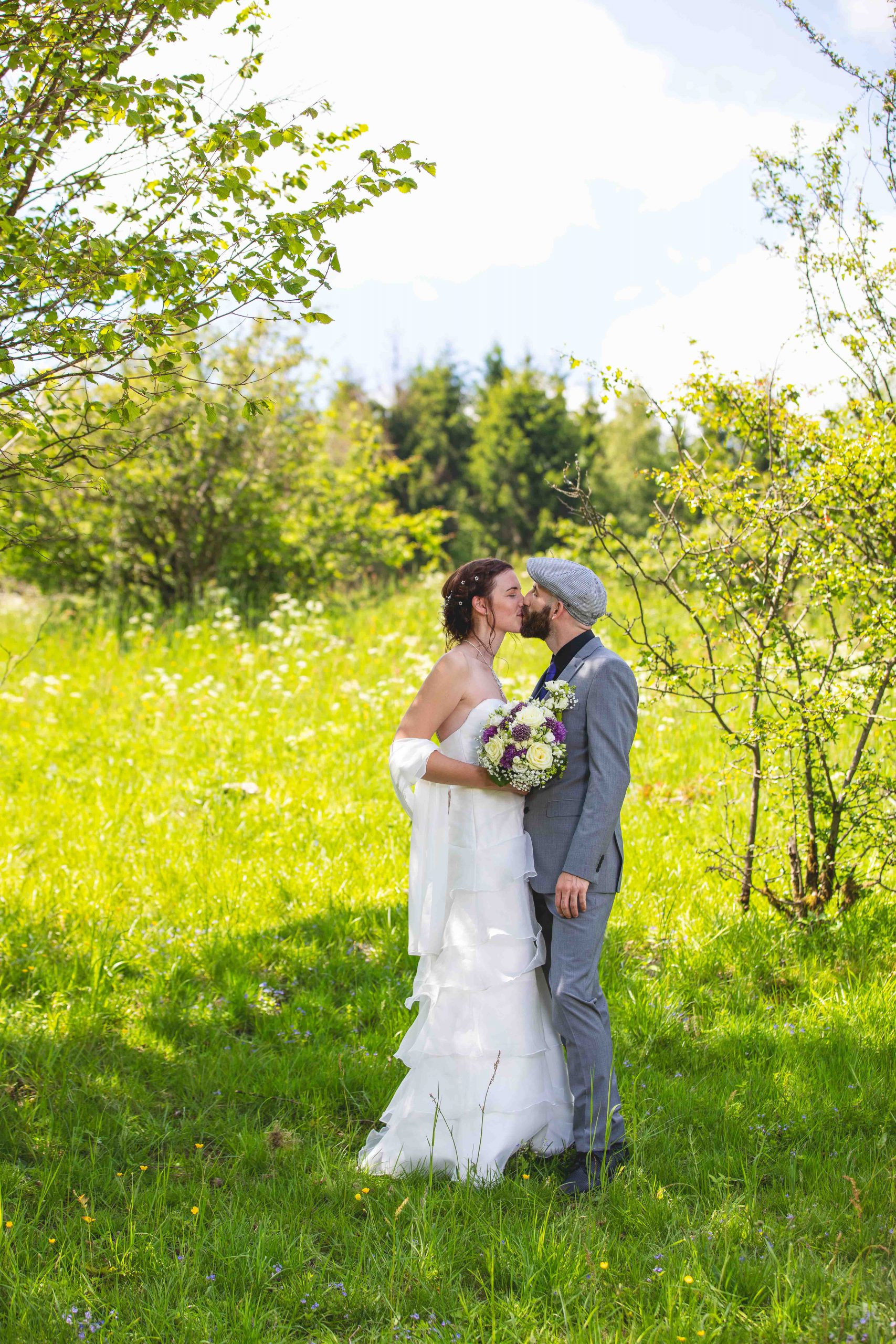 Hochzeitsfoto eines küssenden Brautpaares auf einer Wiese